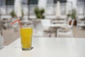 Glass of orange juice with plastic straw on white table in restaurant outdoor lounge zone Royalty Free Stock Photo