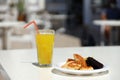 Glass of orange juice with plastic straw on white table in restaurant outdoor lounge zone Royalty Free Stock Photo