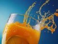 A glass of orange juice with splashes and a slice of orange inside on a blue background close-up Royalty Free Stock Photo