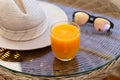 A glass of orange juice, sunglasses and a grey hat are on a table lit by sunlight. Royalty Free Stock Photo