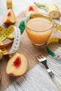 A glass of peach juice on a sackcloth on a white wooden table with slices of fruit and a fork and a centimeter Royalty Free Stock Photo