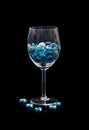 A glass on a stem with shiny glass stones of aquamarine color on a black background