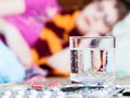 Glass and pills on table close up and sick woman