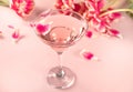 Glass of pink cocktail with flowers and petals. Birthday party or Valentines day romatic couple concept.