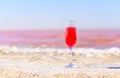 A glass with a pink drink on the white shore of a pink lake. Fabulous and romantic atmosphere.
