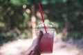 Glass of pink lemonade on hot summer day. Female hand holds plastic glass with straw.