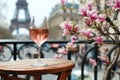 Glass of pink wine on a table of typical Parisian outdoor cafe with pink magnolia flowers in full bloom on a backdrop of French