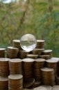 Glass planet on big pile of shiny ukrainian old 1 hryvnia coin stacks close up on blurred green trees background. The concept of