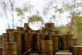 Glass planet on big pile of shiny ukrainian old 1 hryvnia coin stacks close up on blurred green trees background. The concept of