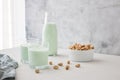 A glass of plant-based nut milk is on the table next to a bottle of pistachio milk and pistachios. The perfect drink for