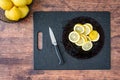 Glass plate with fresh lemon slices, and paring knife, on a black cutting board, wood table, basket of lemons