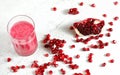 Glass with pomegranate smoothie, gem like fruits scattered next to in on white board desk, view from above