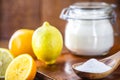 Glass pot with baking soda and wooden measuring spoon, with fruits in the background, lemon and orange, chemical compound used in