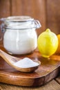 Glass pot with baking soda and wooden measuring spoon, with fruits in the background, lemon and orange, chemical compound used in