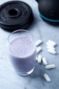 Glass of Protein Shake with milk and blueberries. Creatine capsules, black sporting kettlebell and plates in background. Sport nut Royalty Free Stock Photo