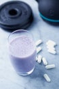 Glass of Protein Shake with milk and blueberries. Creatine capsules, black sporting kettlebell and plates in background. Sport nut Royalty Free Stock Photo