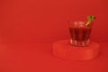 A glass of red cocktail with greens on the podium. Stylish alcohol tomato beverage Bloody Mary on a red background Royalty Free Stock Photo