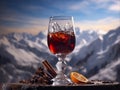 a glass of red drink with pieces of ice stand with dried spices, a slice of orange against a background of snow-capped mountains