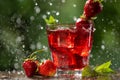 In a glass a red drink with strawberries, mint and ice cubes, in backlight, water drops and splashes, summer concept Royalty Free Stock Photo