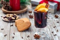 Glass of red glogg or mulled wine with orange slices and cinnamon stick, gingerbread cookies and gift box on background,
