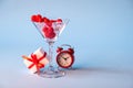 Glass with red heart shaped sugar candy and ice. Gift box and Red alarm clock on a blue background. Time for love. Royalty Free Stock Photo