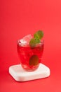 Glass of red refreshing drink with mint on red background. Colorful summer non-alcoholic refreshing drink with ice or fruit iced Royalty Free Stock Photo