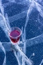 A glass with red tincture stands on the ice of a lake with beautiful cracks.