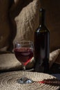 A glass of red wine on a background of burlap. Bottle of red wine.