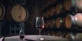 Glass of red wine on background of wooden oak barrels in cellar of winery Royalty Free Stock Photo