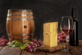 A glass of red wine with a bottle, a wine barrel, a large piece of cheesse, grapes, and vine leaves Royalty Free Stock Photo