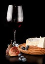 A glass and a bottle of red wine, brie cheese on a wooden plate, fresh figs and blueberries on a dark table Royalty Free Stock Photo