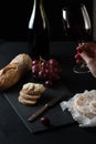 Glass of red wine with a bottle, cluster of grapes, women hand placing brie cheese to rustick piece of bread with antique knife. Royalty Free Stock Photo