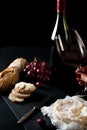 Glass of red wine with a bottle, cluster of grapes, women hand placing brie cheese to rustick piece of bread with antique knife. Royalty Free Stock Photo