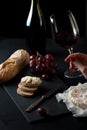 Glass of red wine with a bottle, cluster of grapes, women hand placing brie cheese to rustick piece of bread with antique knife. Royalty Free Stock Photo