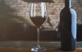 Glass of red wine and wine bottle on colorful wooden table at home, brick wall in the background Royalty Free Stock Photo