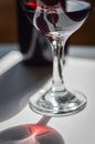 Glass of red wine and bottle with shadows and reflections on a white textured surface. Royalty Free Stock Photo