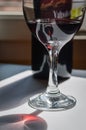 Glass of red wine and bottle with shadows and reflections on a white textured surface. Royalty Free Stock Photo