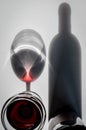 Glass of red wine and bottle with shadows and reflections on a white textured surface. Royalty Free Stock Photo