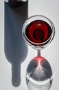 Glass of red wine and bottle with shadows and reflections on a white textured surface. Royalty Free Stock Photo