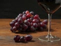 Glass of red wine and cluster of red grapes on a wooden table, dark background. Selective focus Royalty Free Stock Photo