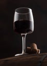 Glass of red wine with corks on top of wooden barrel on black