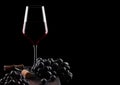 Glass of red wine with dark grapes and vintage corkscrew opener and cork on wooden board on black background. Space for text Royalty Free Stock Photo