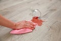 Glass of red wine fell on laminate, wine spilled on floor. A woman wipes the laminate from moisture. Royalty Free Stock Photo