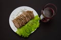 Glass of red wine and fork sliced pork meat with lettuce leaves on a plate Royalty Free Stock Photo