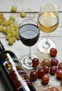 Two glasses of wine and a bottle on a wooden table surrounded by grapes