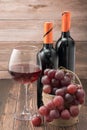 Glass of red wine with grapes on wooden table against the background of bottles Royalty Free Stock Photo