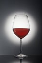 Glass with red wine on a gray background with backlight and reflection