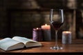 Glass of red wine, open book with candles in the background on wooden table