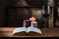 Glass of red wine, open book with candles in the background on wooden table