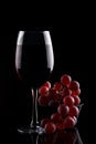 A glass of red wine and red grapes on a black background.